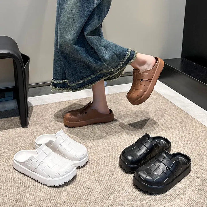 A woman wearing stylish brown EVA clogs with a woven upper, styled with denim jeans, while other pairs in white and black are displayed on a rug.