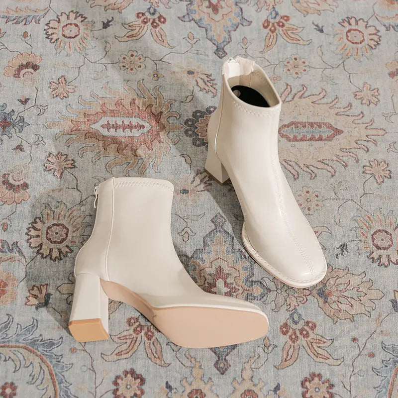 Kalyx white faux leather ankle boots with a chunky block heel and square toe, shown from a three-quarter angle on a patterned rug.