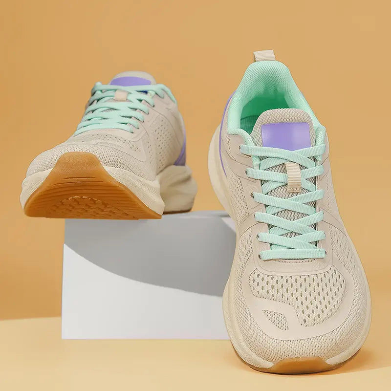 Pair of wide-fit athletic trainers in beige engineered mesh with mint green laces and purple accents, shown from a three-quarter angle on a white pedestal.