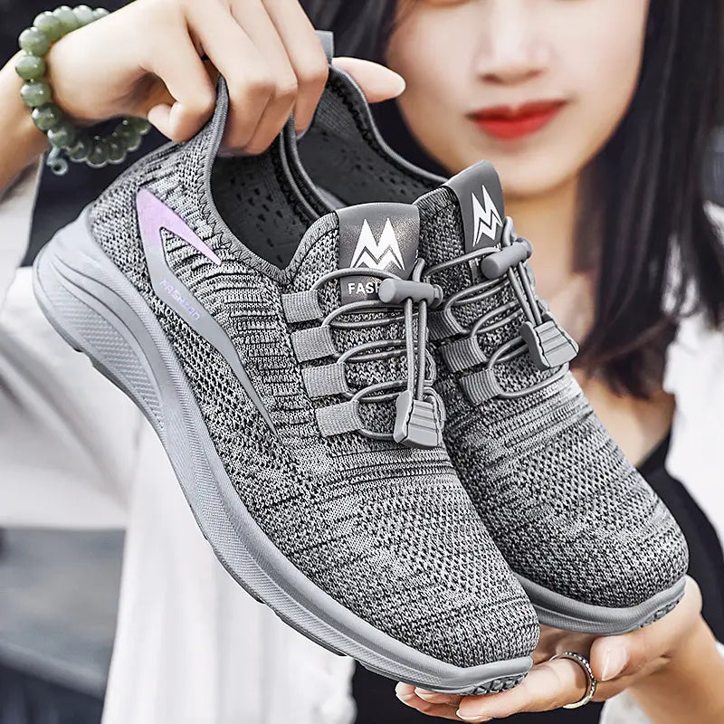Kaviri women's grey breathable knit sneakers with quick-tie elastic laces, held by hands against a soft-focus background.
