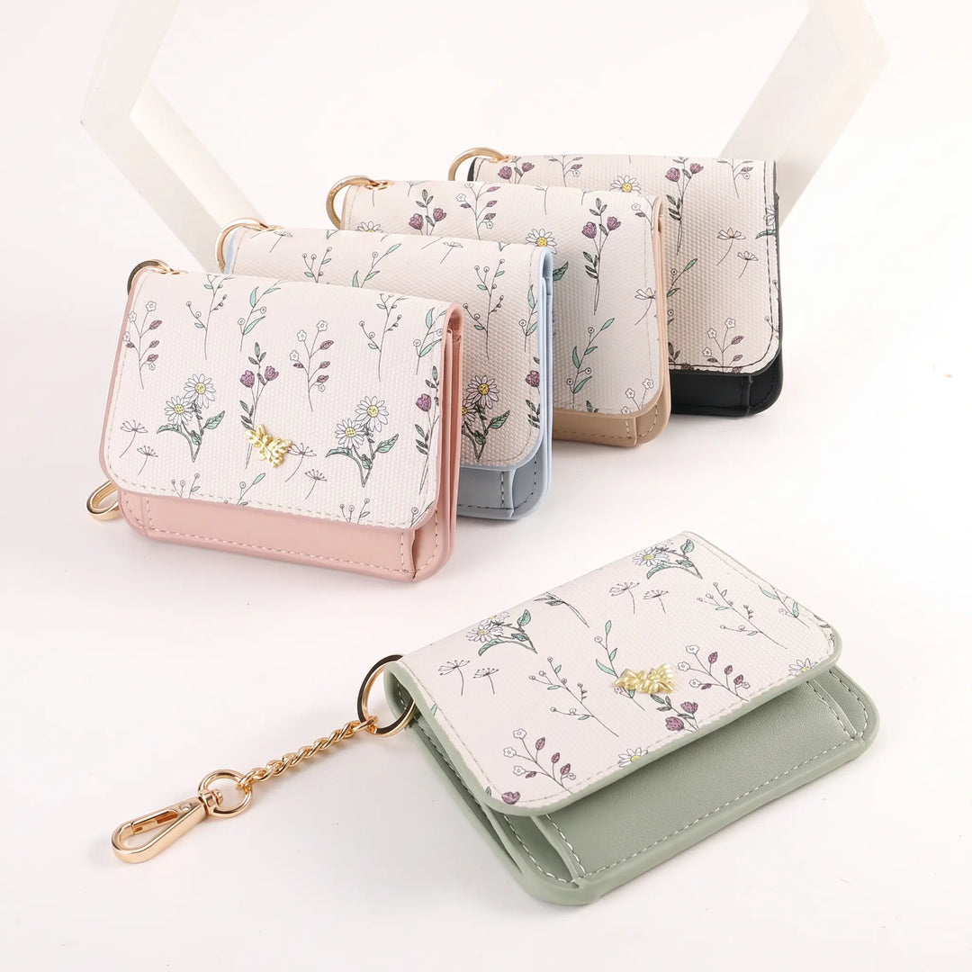 Collection of Kezel compact tri-fold wallets featuring a delicate floral print on PU leather, with gold-tone hardware and keychains, displayed on a white studio background.