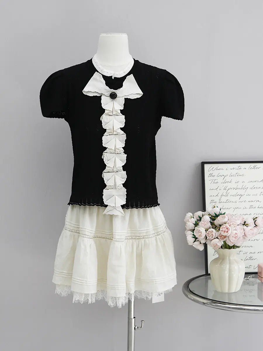 Black Kezh short sleeve knit top with white cascading ruffle trim, black bow accent, and scalloped hem, displayed on a mannequin.