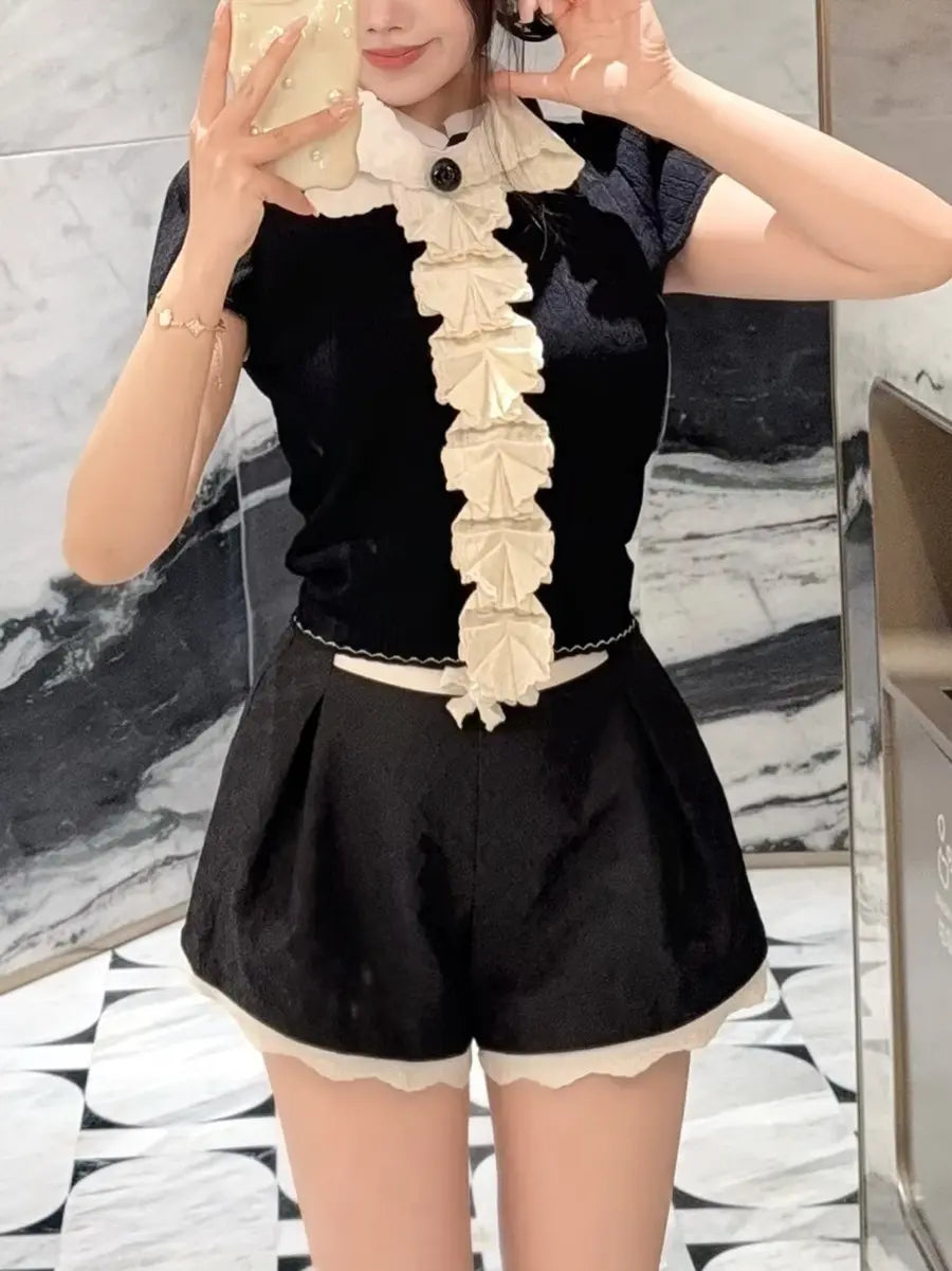 Kezh black short sleeve knit top with white cascading ruffle trim and black bow accent, worn by a model with black shorts.