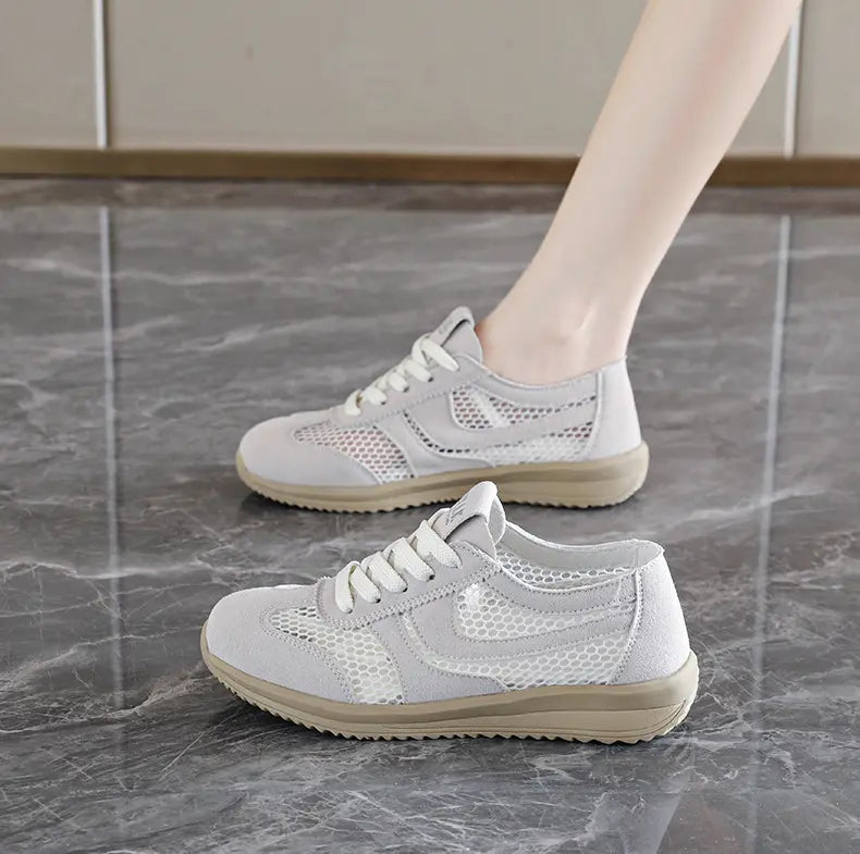 Grey breathable mesh low-top trainers with suede-like accents, worn on a foot in a casual lifestyle setting on a marble-effect floor.