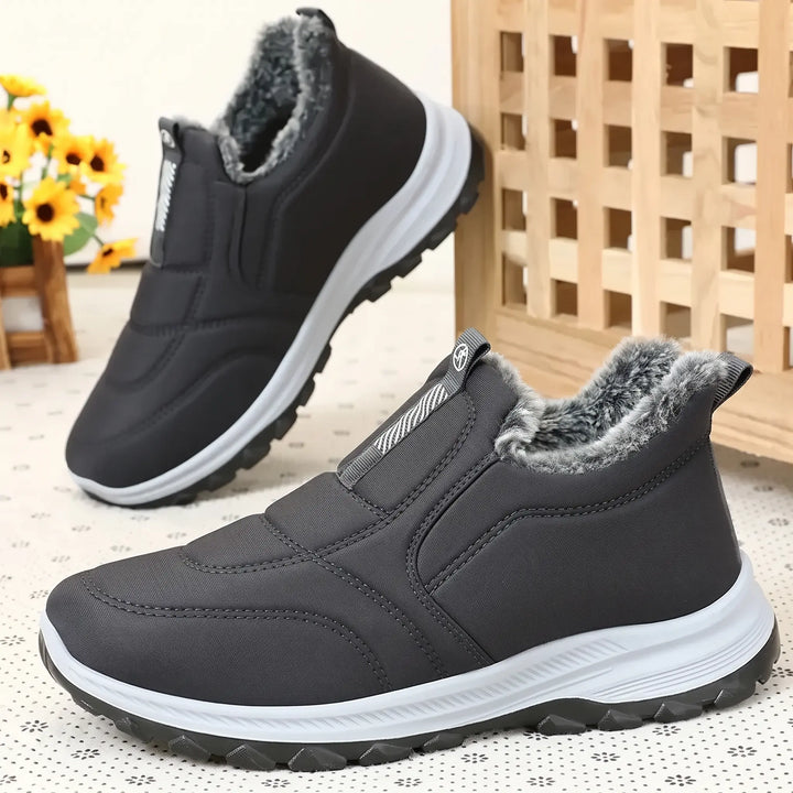A pair of dark grey, mid-calf winter boots with a quilted Lycra upper and fluffy faux fur lining. Shown from multiple angles on a patterned background with decorative elements.