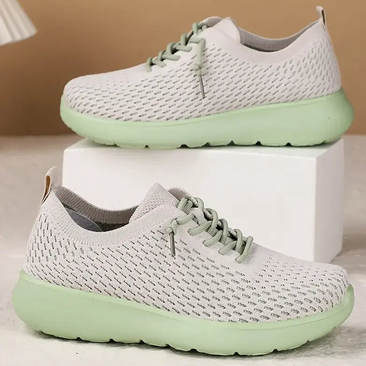 Two light grey breathable knit trainers with mint green soles and laces, displayed stacked in a studio setting.