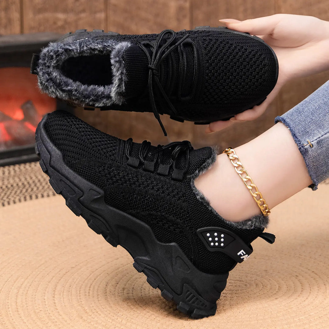 Close-up of black Kryptik ankle boots with plush faux fur lining and a chunky platform sole, shown on a foot with a gold anklet.