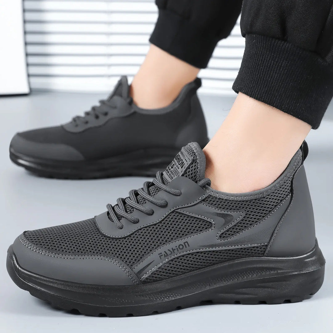 Men's Krythos breathable mesh trainers in stealth grey, shown from the side with embossed 'FASHION' detailing and a sculpted polyurethane sole. Features a lace-up closure and padded collar for comfort.