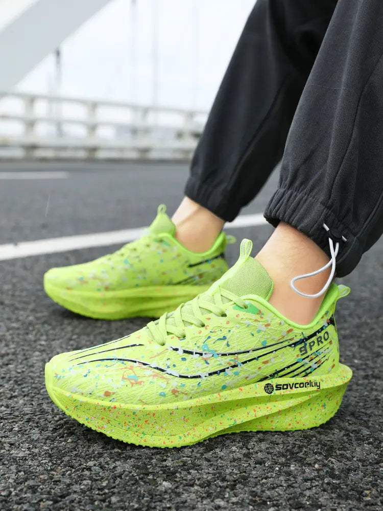 Vibrant green Krytox running shoes with artistic multi-color paint splash pattern and black accent lines, shown on feet in an outdoor setting with a sculpted, speckled midsole.
