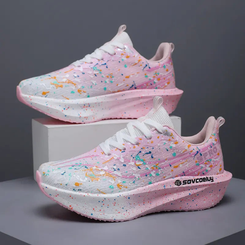 Pair of Krytox performance running shoes with vibrant pink and white paint splash pattern, sculpted pink speckled midsole, and white laces. Side view of avant-garde speed trainers.