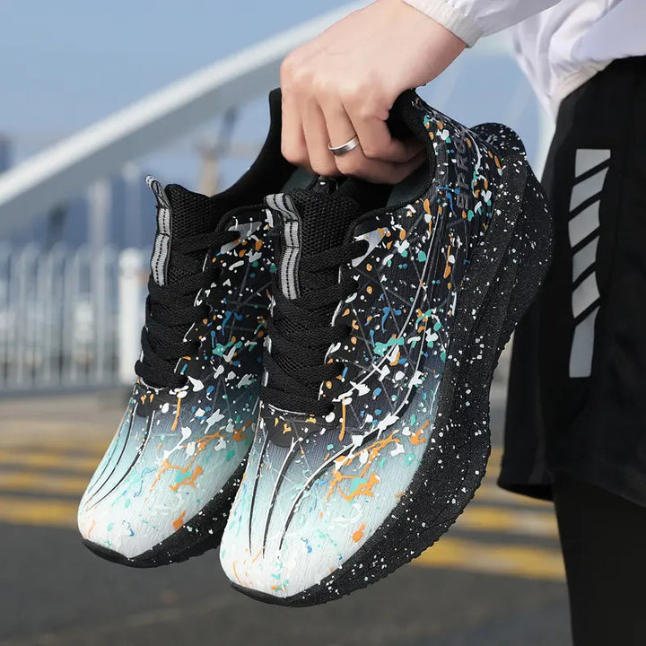 Performance running shoes with vibrant multi-color paint splash design on engineered mesh uppers, held by hand showing a three-quarter view of the sculpted, speckled midsole and outsole.