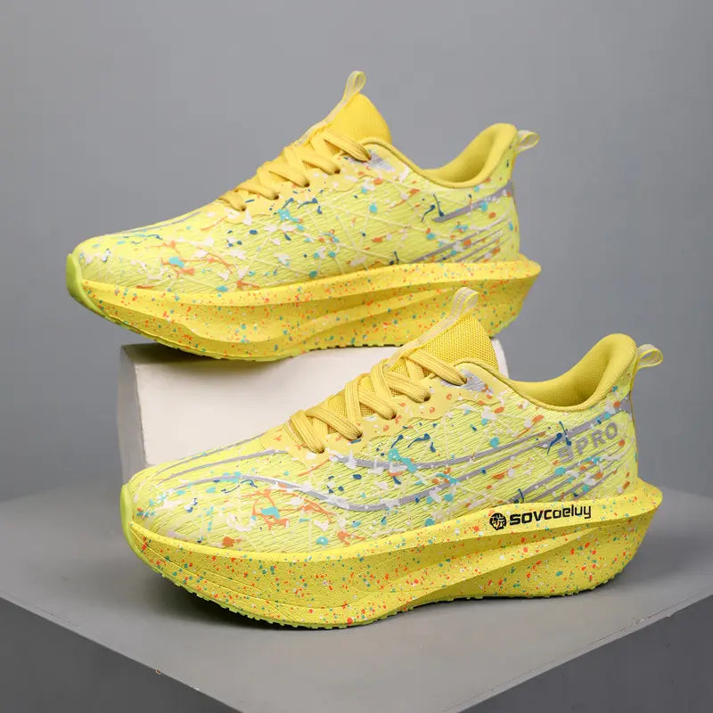 Two yellow Krytox performance running shoes with vibrant multi-color paint splash patterns displayed on a studio surface. The shoes feature sculpted, speckled midsoles and side branding.