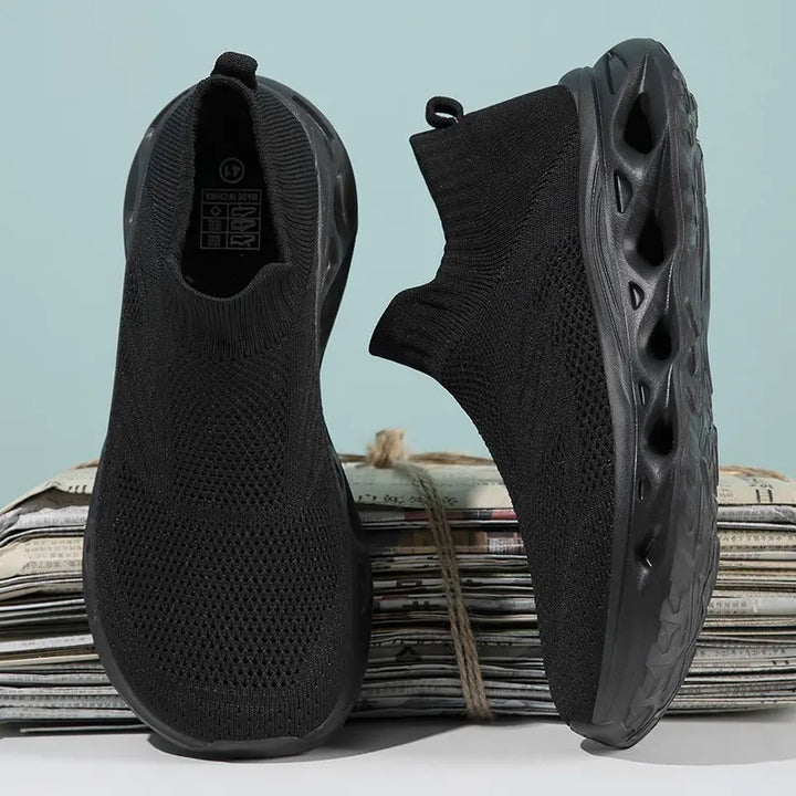 Pair of black Kryxis knit slip-on sneakers with sock-like fit and sculpted wave-patterned soles, shown from a front three-quarter angle.