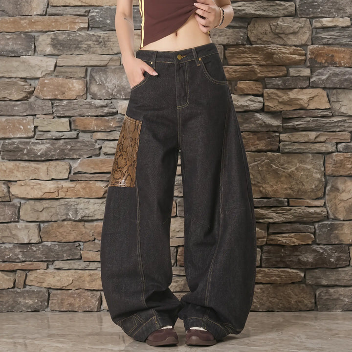 Front view of Kylath wide leg jeans featuring a striking snake print panel on the left thigh, dark wash denim, and visible tonal stitching, presented on a model.