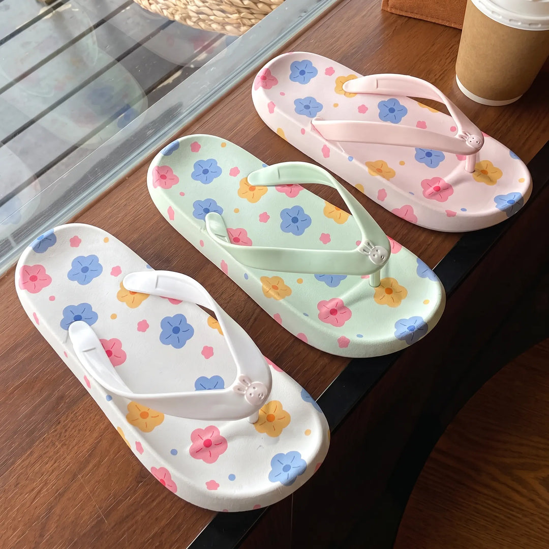 Three pairs of Kythor floral platform flip-flops in pastel white, green, and pink, featuring a bunny charm on each thong strap and vibrant flower patterns on the footbeds.