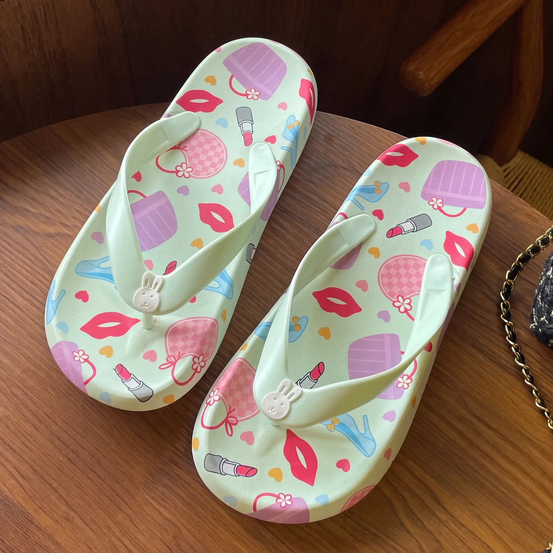 Kythor pastel green platform flip-flops adorned with a playful pattern of lipstick, lips, and handbags, featuring a cute bunny charm on the toe post.