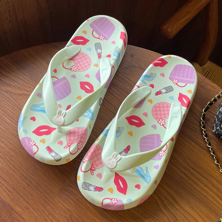 Kythor pastel green platform flip-flops adorned with a playful pattern of lipstick, lips, and handbags, featuring a cute bunny charm on the toe post.