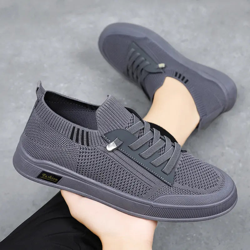 Grey Kyzir men's breathable mesh casual sneakers shown in a three-quarter profile view, held in a hand, with a white rubber sole and subtle side accent.