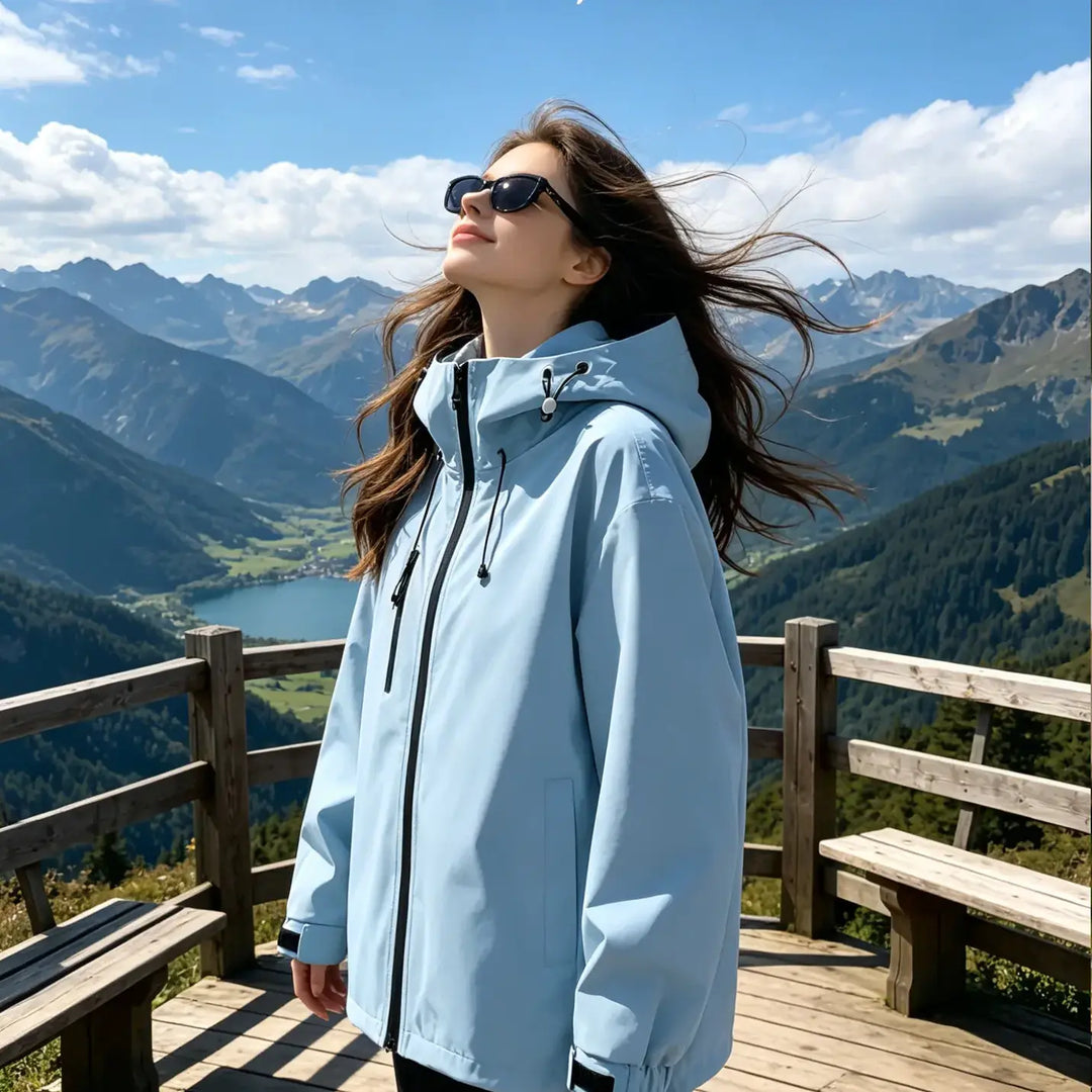 Woman wearing a light blue hooded waterproof jacket in a scenic mountain setting, looking up at the sky with windblown hair, text overlay "BREATHE DEEP, LIVE SLOW".