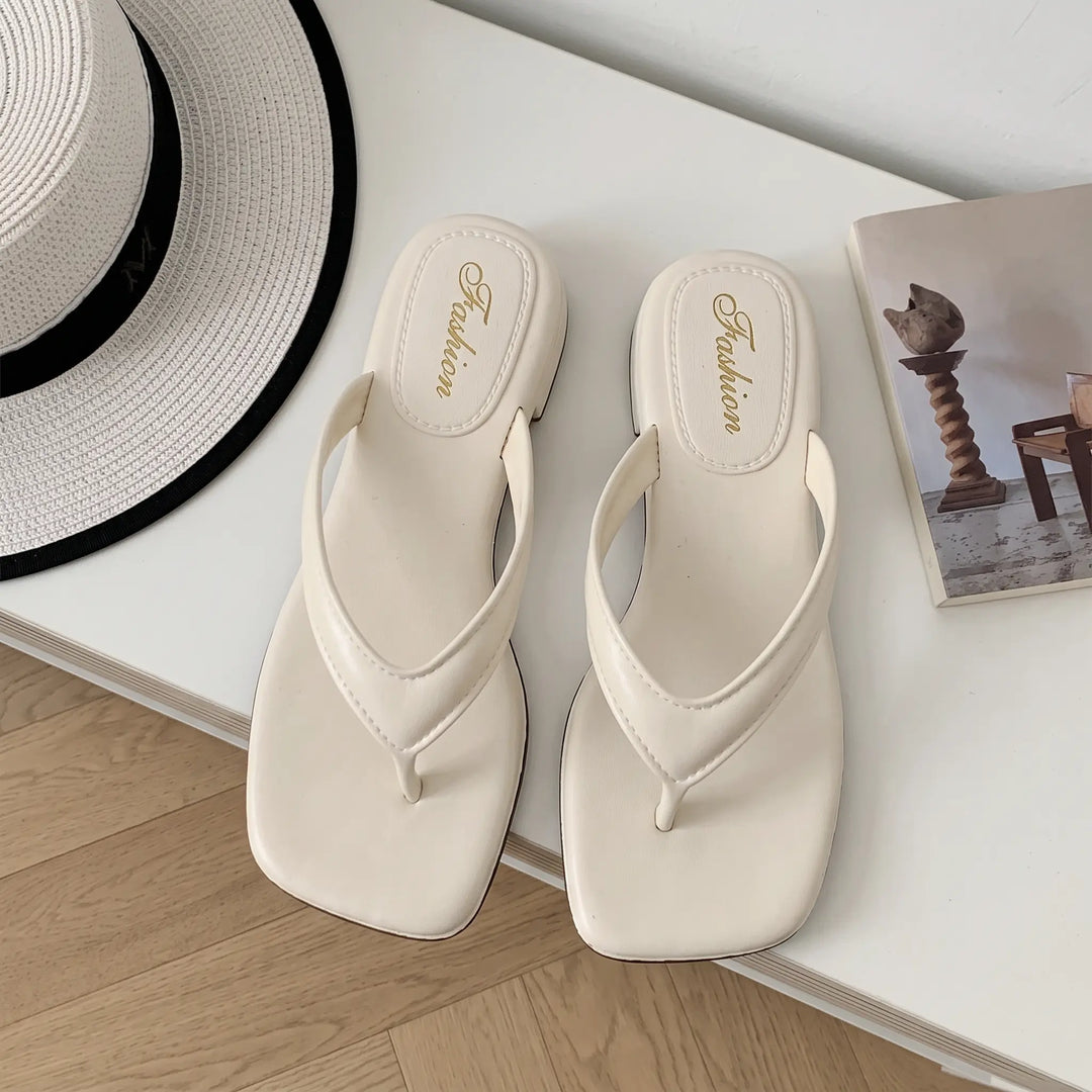 A pair of light ivory square-toe thong sandals with a subtle embossed &