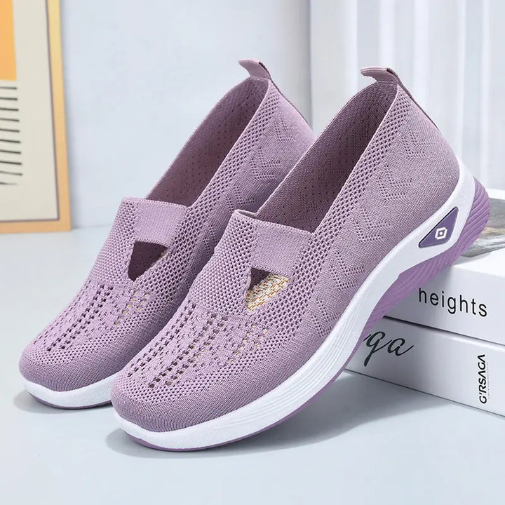 A pair of light purple breathable knit slip-on sneakers with a geometric weave pattern and white cushioned midsole shown from a three-quarter angle.