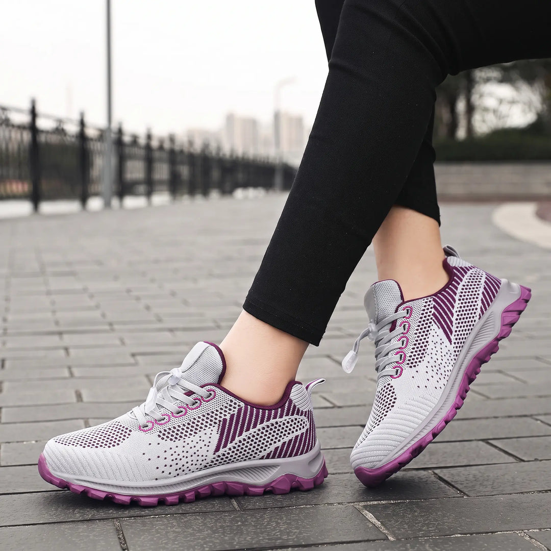 Lightweight grey and purple knitted mesh walking trainers shown on feet in a lifestyle outdoor setting, featuring a quick-lace toggle system and patterned outsole.
