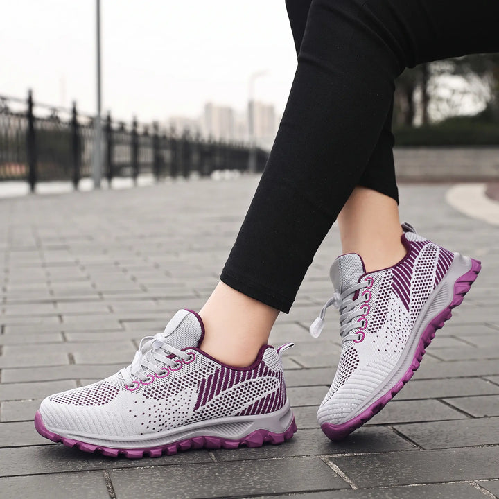 Lightweight grey and purple knitted mesh walking trainers shown on feet in a lifestyle outdoor setting, featuring a quick-lace toggle system and patterned outsole.