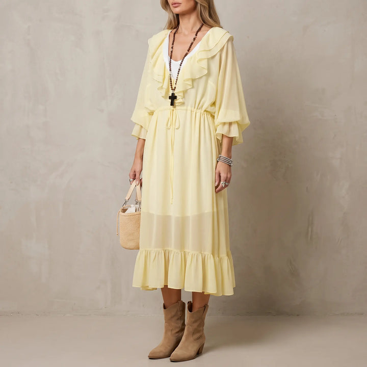 A pale yellow chiffon midi dress with cascading ruffles on the V-neck, voluminous sleeves, and tiered hem, worn by a model in a bohemian-chic style with accessories and suede boots.