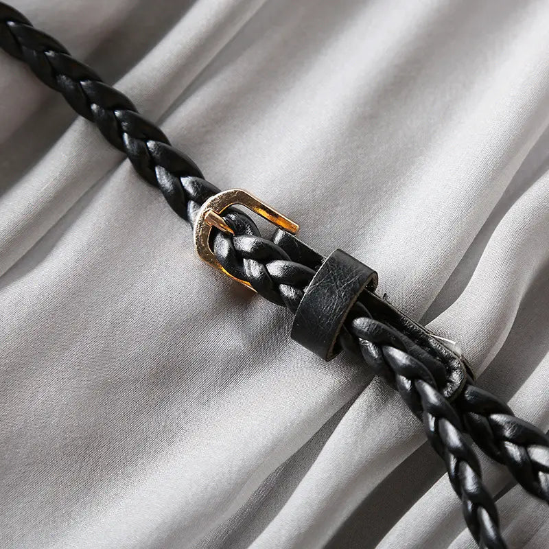 Close-up of the braided black leather belt with a small gold buckle, showcasing the artisan craftsmanship on a muted grey silk dress.