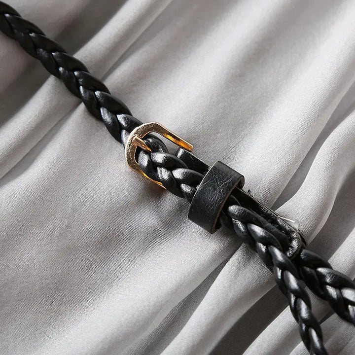 Close-up of the braided black leather belt with a small gold buckle, showcasing the artisan craftsmanship on a muted grey silk dress.