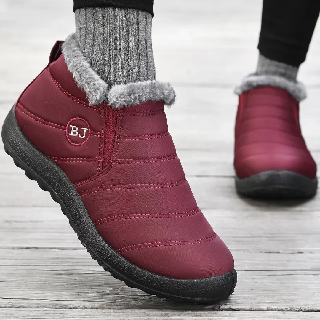 Three-quarter view of maroon quilted winter boots with grey faux fur lining and a black lugged sole, featuring a small embroidered &