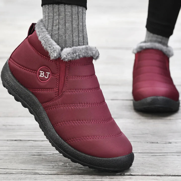 Three-quarter view of maroon quilted winter boots with grey faux fur lining and a black lugged sole, featuring a small embroidered &