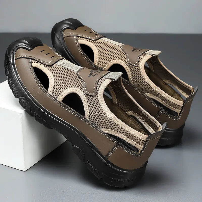 Men's taupe-brown and beige outdoor sandals in a three-quarter view, featuring breathable mesh panels, synthetic leather overlays, a light grey 'FASHION' embossed strap, and a rugged black sole.