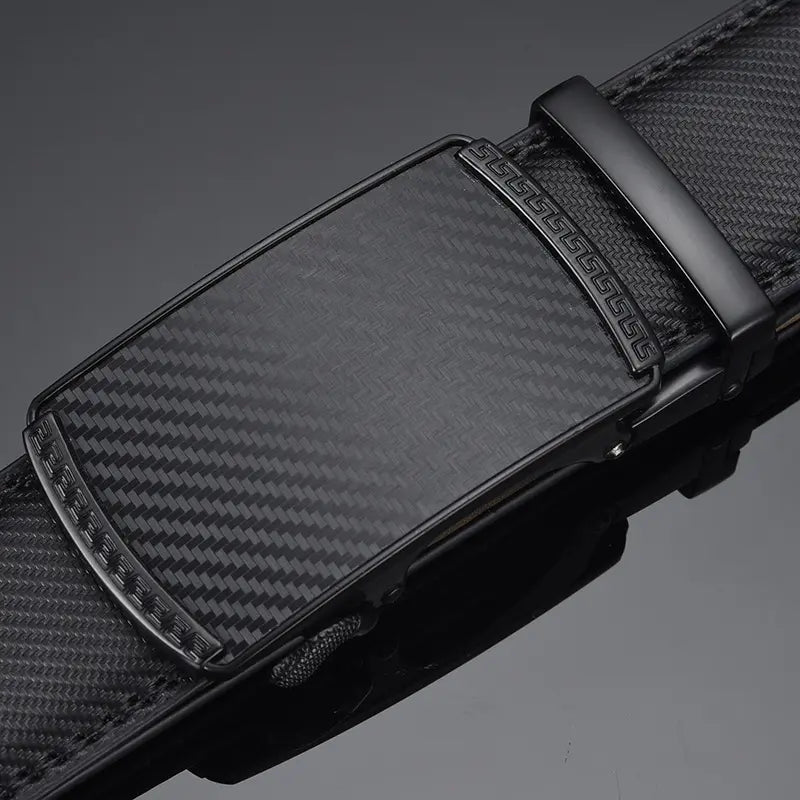 Close-up view of a men's black leather automatic belt, showcasing the matte black alloy buckle with carbon fibre texture and geometric Greek key engraving, and the strap's woven pattern. Black stitching and tan leather lining are visible.