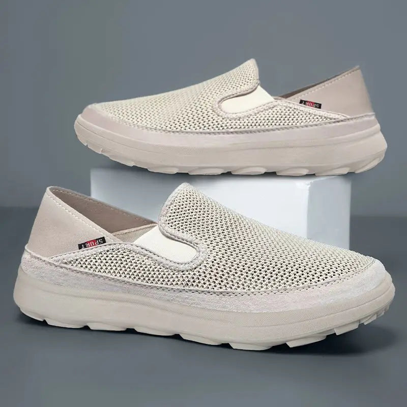 Pair of men's breathable mesh slip-on sneakers in sandy beige, featuring a cushioned sole and elastic side panels for easy wear, shown from a three-quarter side view.