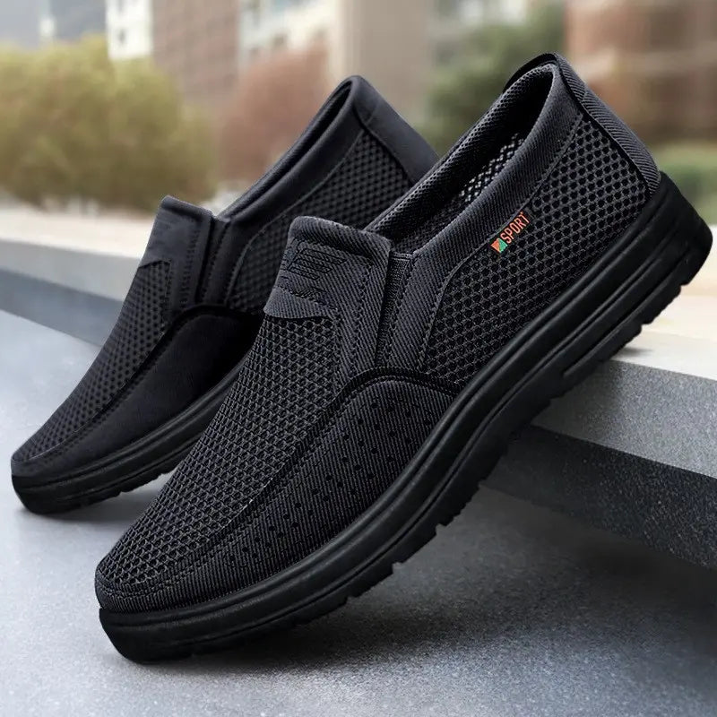 Men's black breathable mesh slip-on loafers with a perforated synthetic toe cap overlay and 'SPORT' accent tag. Features a lightweight, chunky black PVC sole for casual everyday wear.