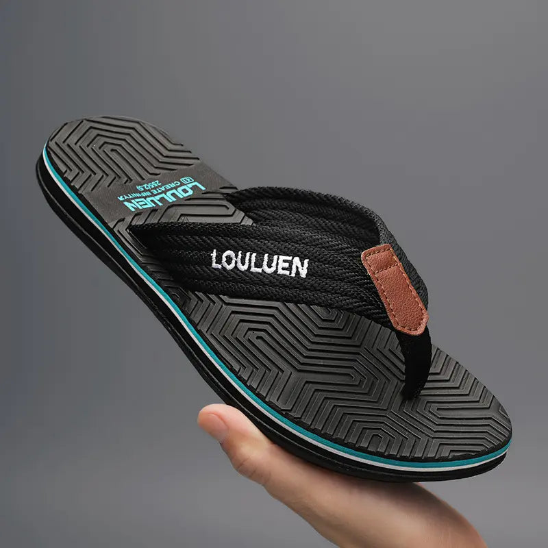 Men's black flip-flop with a textured fabric strap featuring white embroidered 'LOULUEN' text and a small brown leather detail, on a patterned EVA footbed with blue and white sole trim.