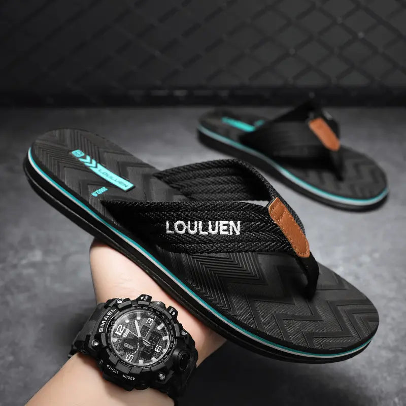 Black men's flip-flops with woven straps and 'LOULUEN' embroidered footbed, displayed on a studio surface with a second sandal in the background.
