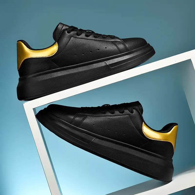 Two black leather men's casual sneakers with a glossy gold heel accent, featuring a thick sculpted sole, presented at a three-quarter angle on a white shelf against a gradient blue backdrop.