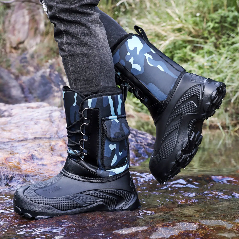 Men's Zanthos high-top winter boots in blue camouflage fabric and black rubber, featuring a lace-up front and side cargo pocket, worn in a rocky, shallow water environment.