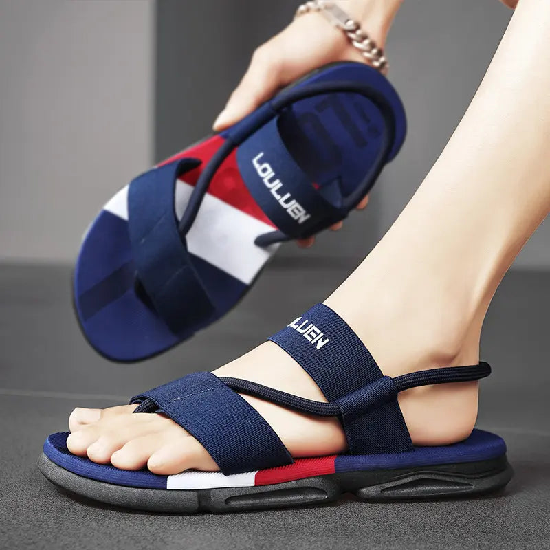 Men's dark blue elasticated strap sandals with white 'LOULUEN' branding, featuring a multi-colored sole stripe of red, white, and grey, shown on a foot in a studio.