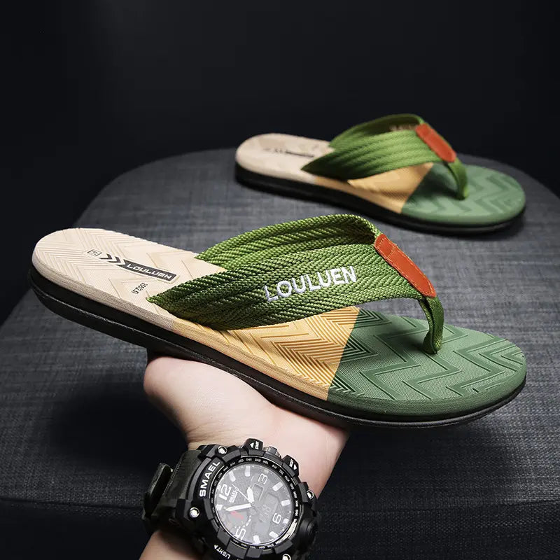 Men's green and yellow Y-strap flip-flops with white 'LOULUEN' embroidery, held in hand against a dark textured background.