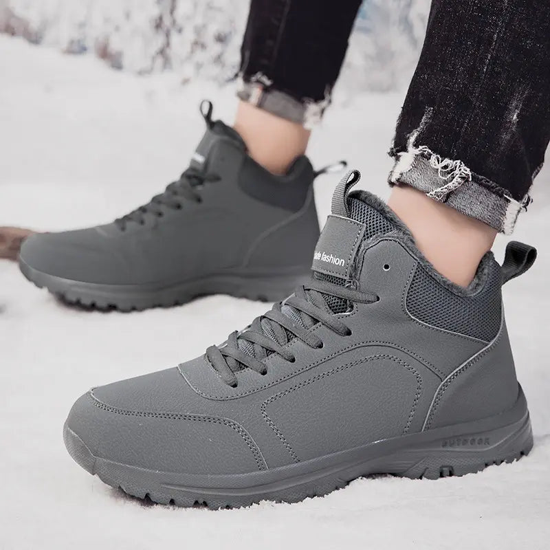 Men's grey mid-top winter boots with plush faux fur lining and a rugged rubber outsole, shown worn in the snow with jeans.