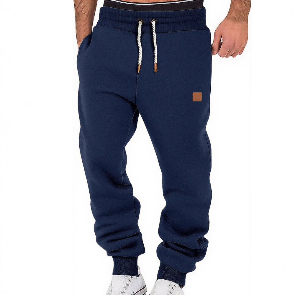 Navy blue men's fleece-lined joggers shown from the front, featuring a tapered fit, ribbed cuffs, drawstring waist, and a subtle square logo patch on the left thigh.