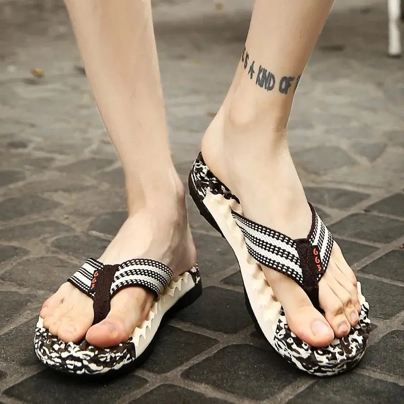 Men's Movae flip-flops worn on feet, showcasing the striped woven straps, contoured footbed, and aggressive tread sole on a paved outdoor surface.
