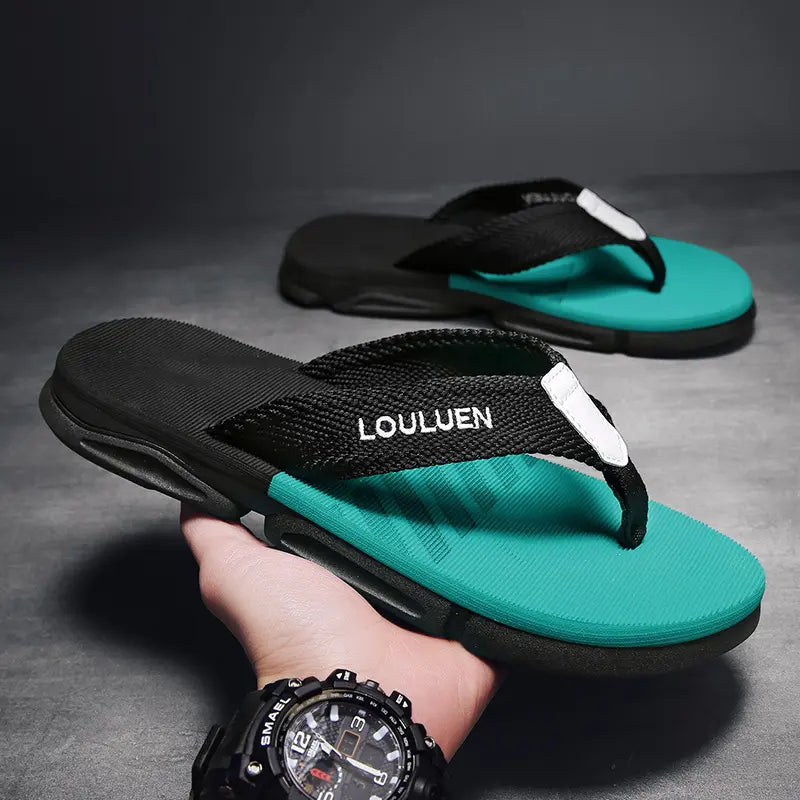 Men's casual flip-flops in turquoise and black, featuring a black fabric strap with white 'LOULUEN' embroidery and a thick, textured EVA footbed. One sandal is held in a hand against a dark grey studio background.