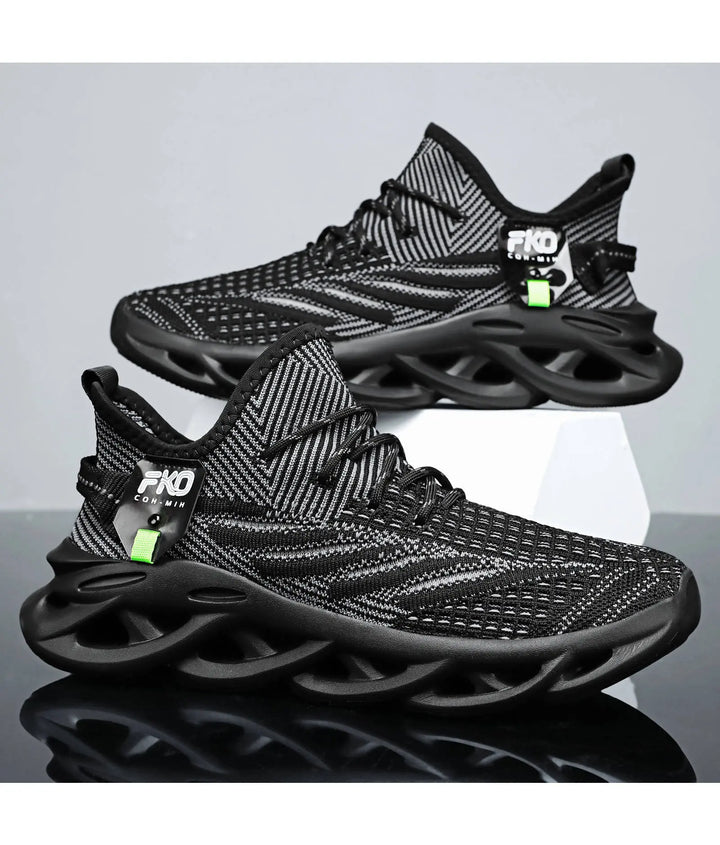 Pair of black and grey Mikari breathable knit sneakers with sculpted dark soles, shown from a three-quarter angle against a studio backdrop. Features a lime green tag and FKO COM-MIH label.