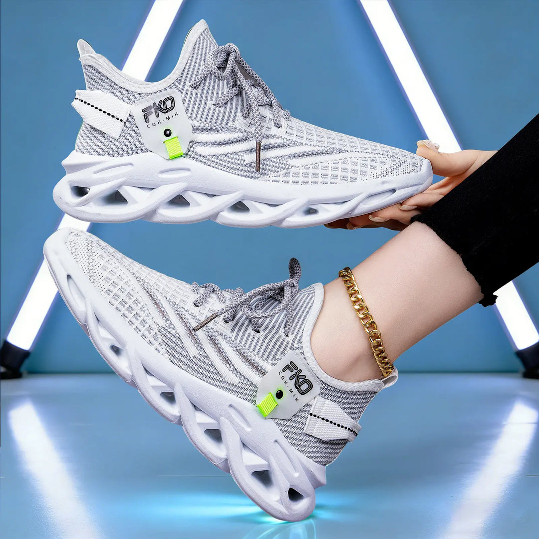Pair of white and grey Mikari breathable knit sneakers shown in a lifestyle shot, one held by hand, the other worn on a foot with a gold anklet, against a stylized blue studio background with geometric lights.