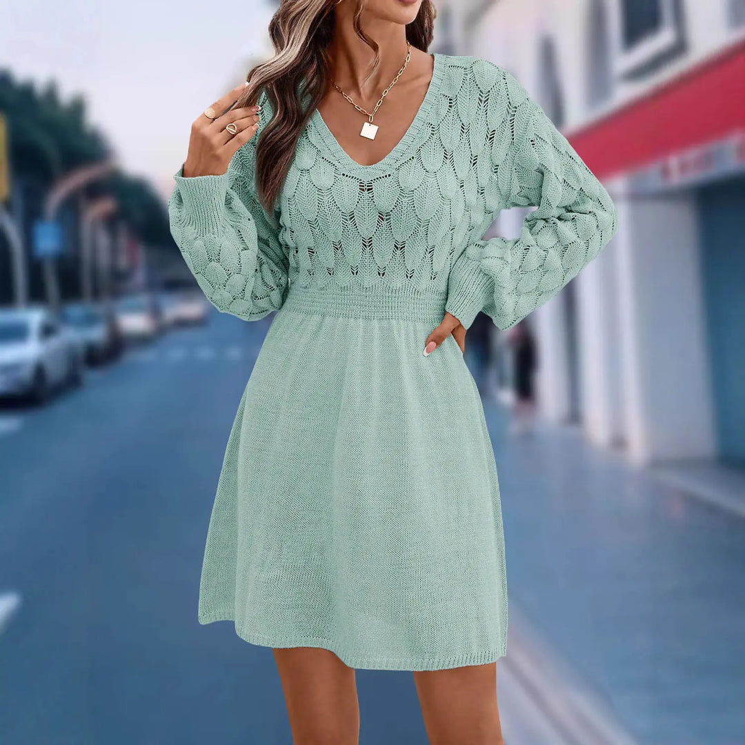 A woman models a misty mint V-neck knit dress featuring an intricate diamond and cable pattern on the bodice and balloon sleeves, cinched elasticated waistband, and a flared A-line skirt.