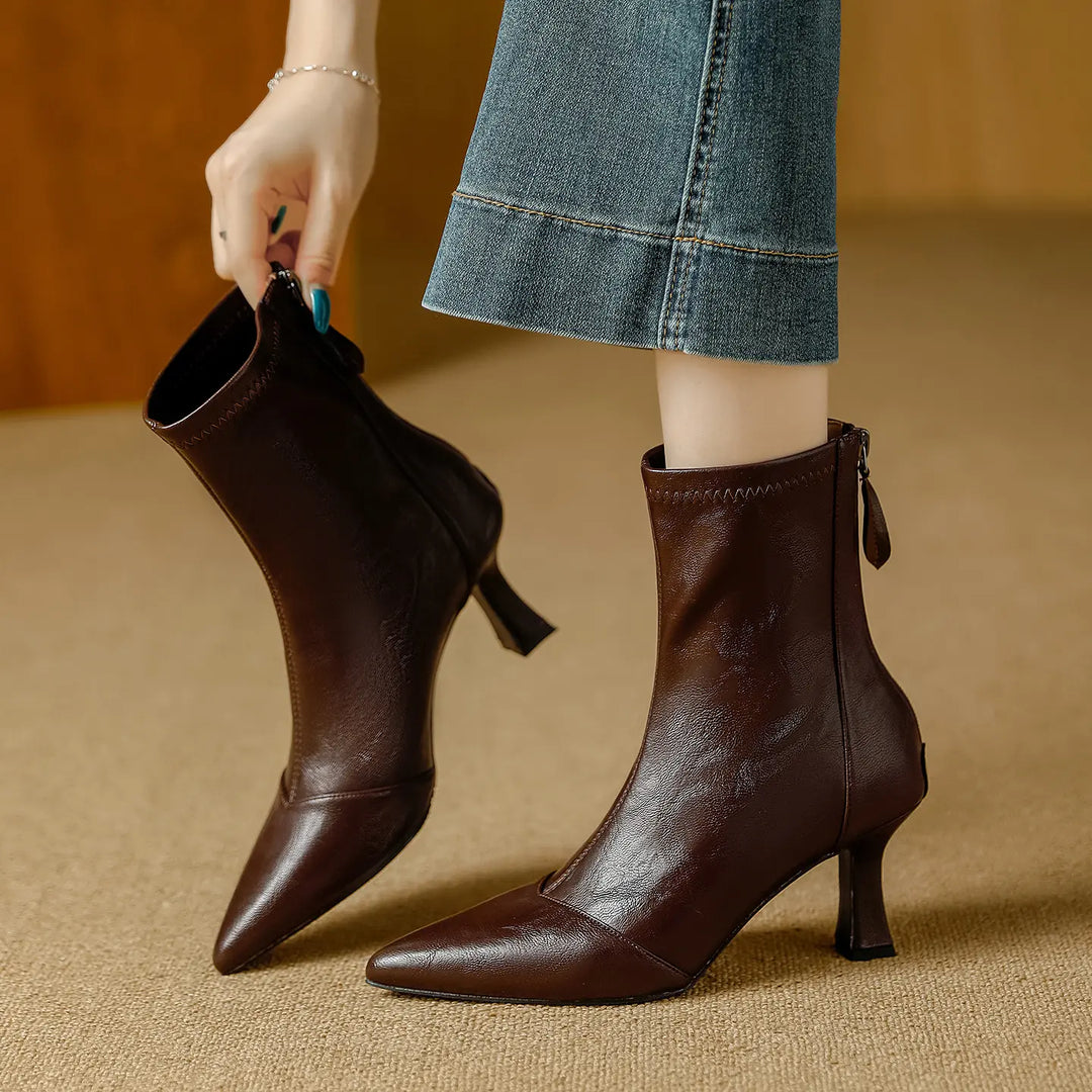 Mizuki chic pointed toe ankle boots in rich chestnut faux leather, shown from the side with a back zipper detail and stiletto heel as a hand pulls one boot on.